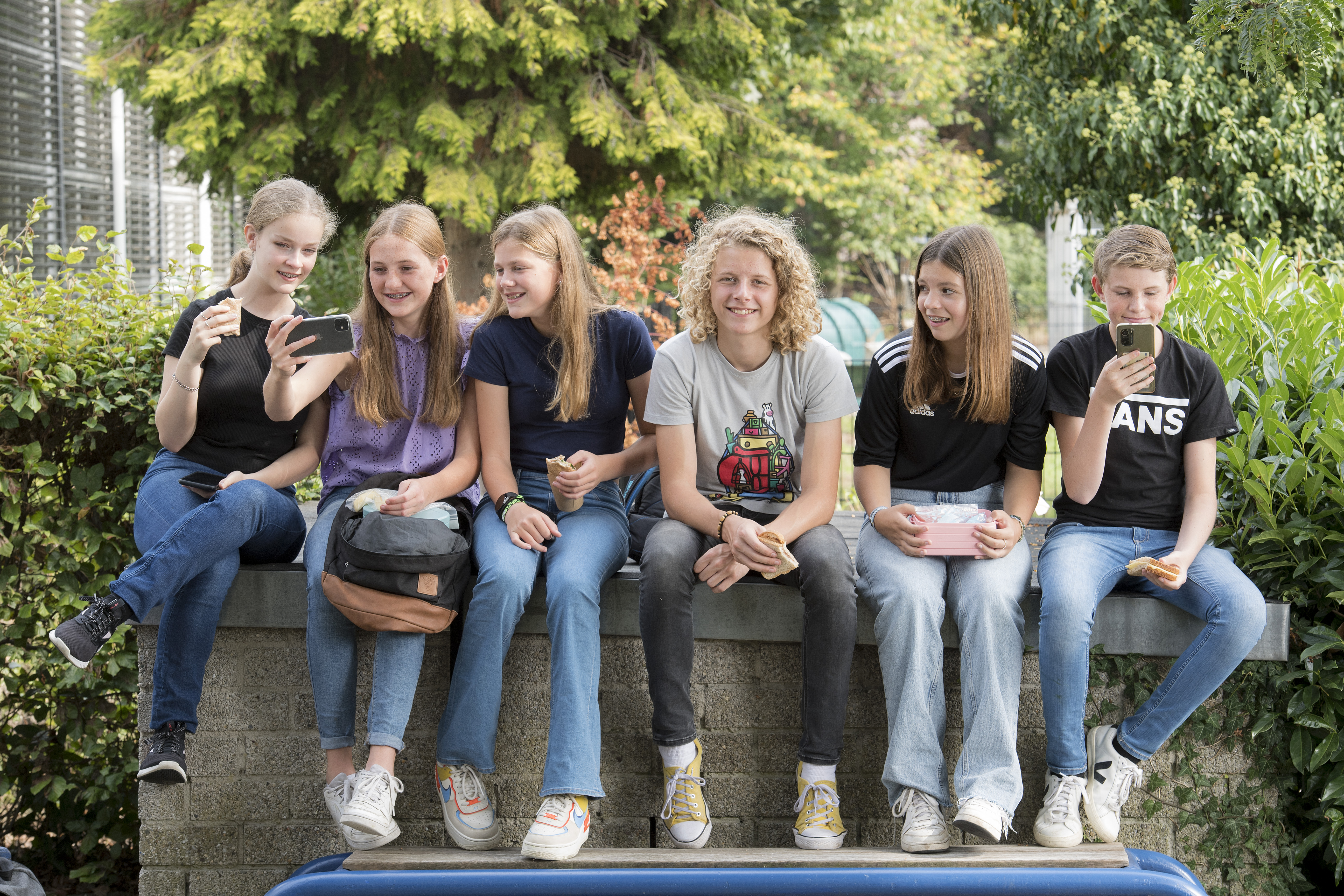 6 leerlingen zitten samen buiten met een groene tuin op de achtergrond