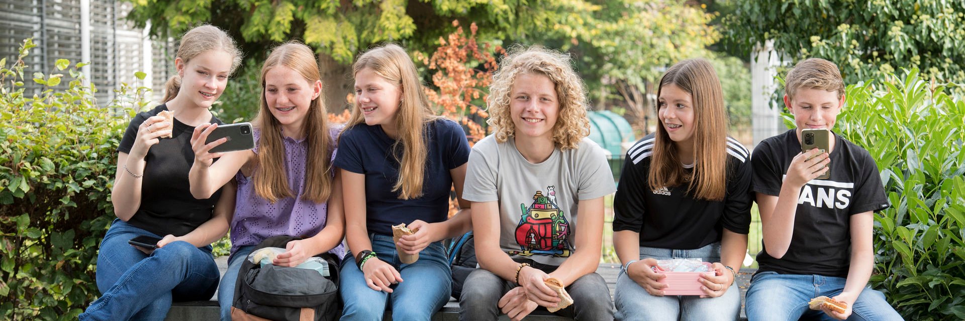 6 leerlingen zitten samen buiten met een groene tuin op de achtergrond