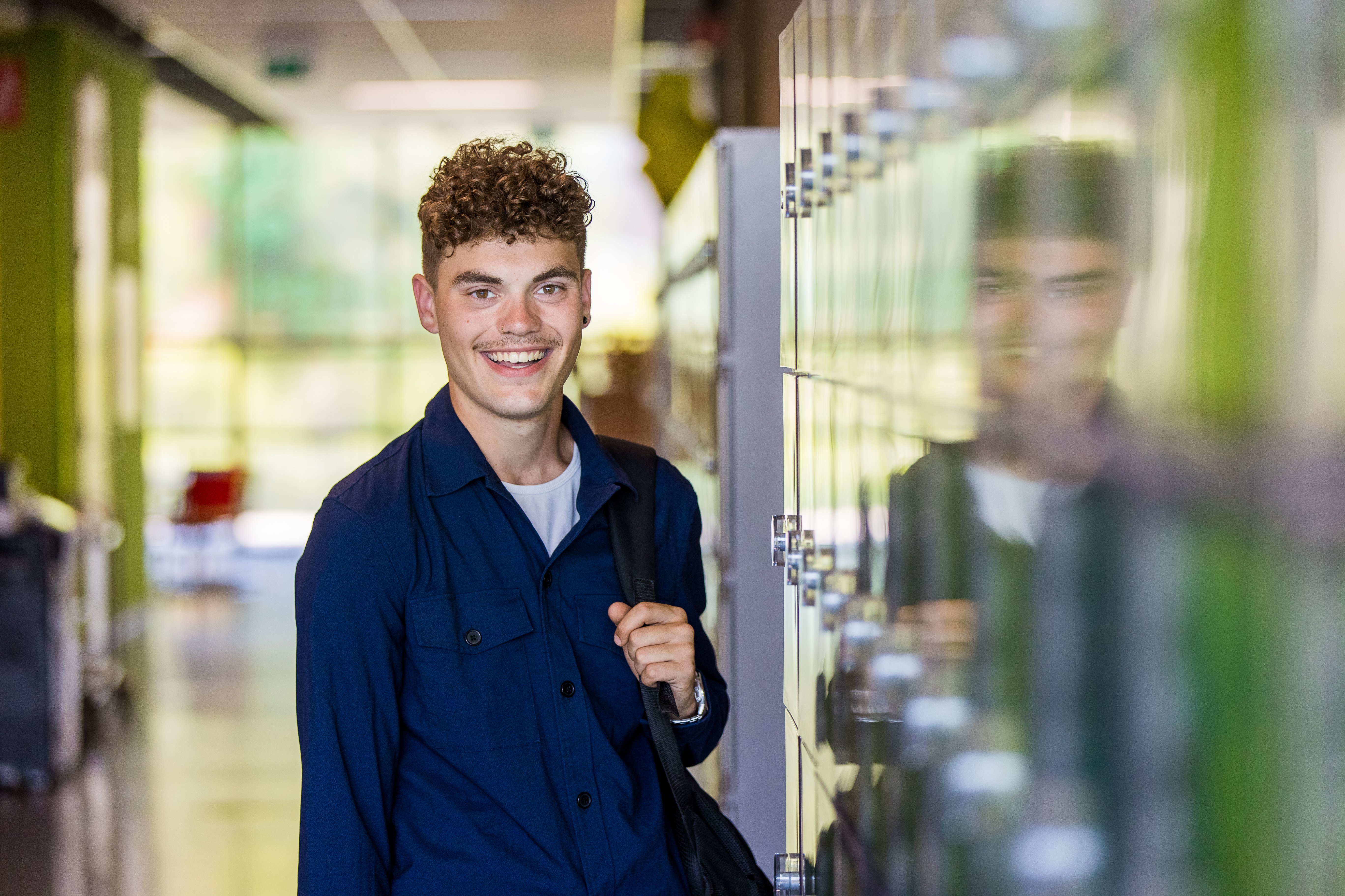 Een student naast kluisjes lacht naar de camera