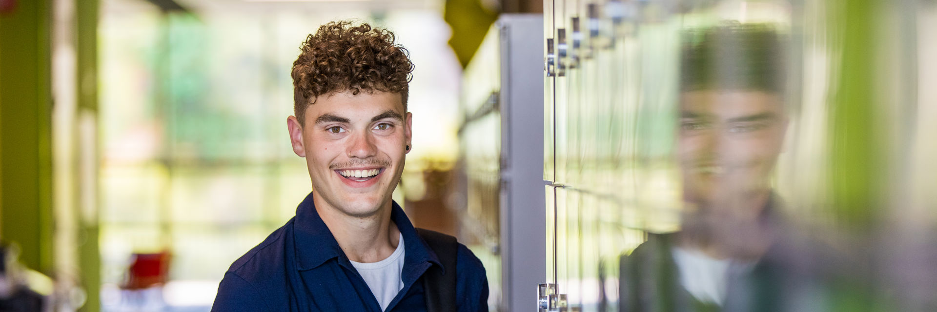 Een student naast kluisjes lacht naar de camera