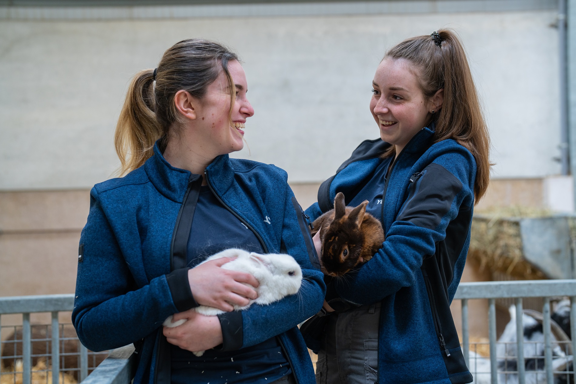 2 meisjes lachend naast elkaar met een konijn op hun arm