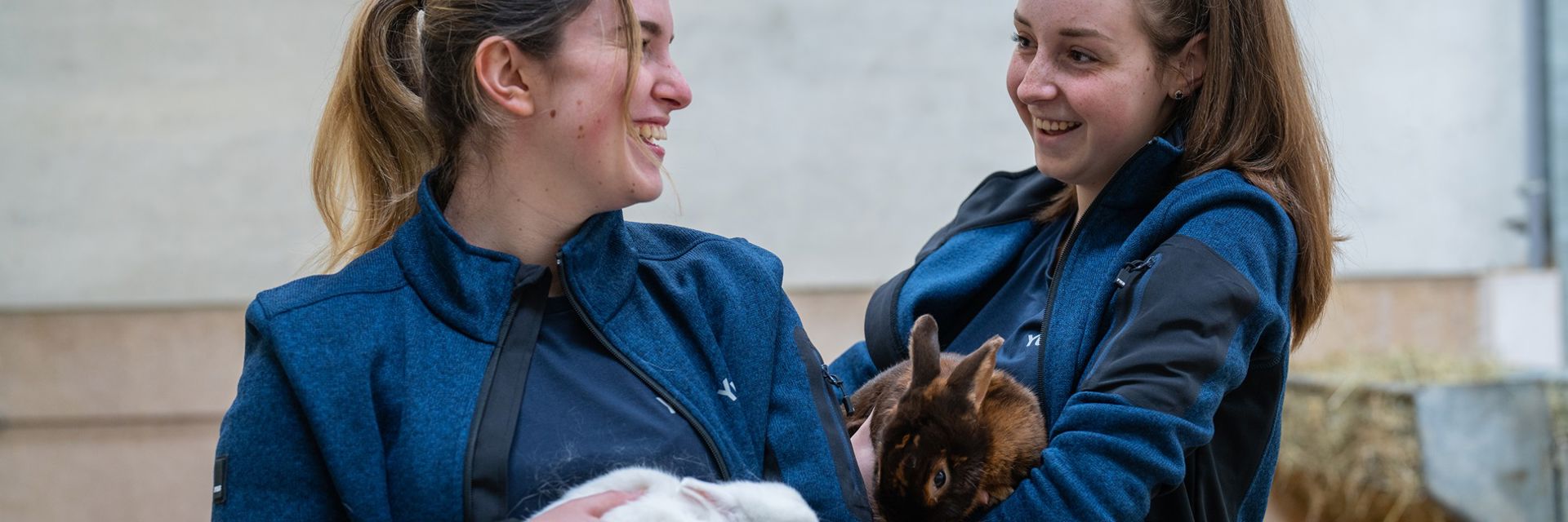 2 meisjes lachend naast elkaar met een konijn op hun arm