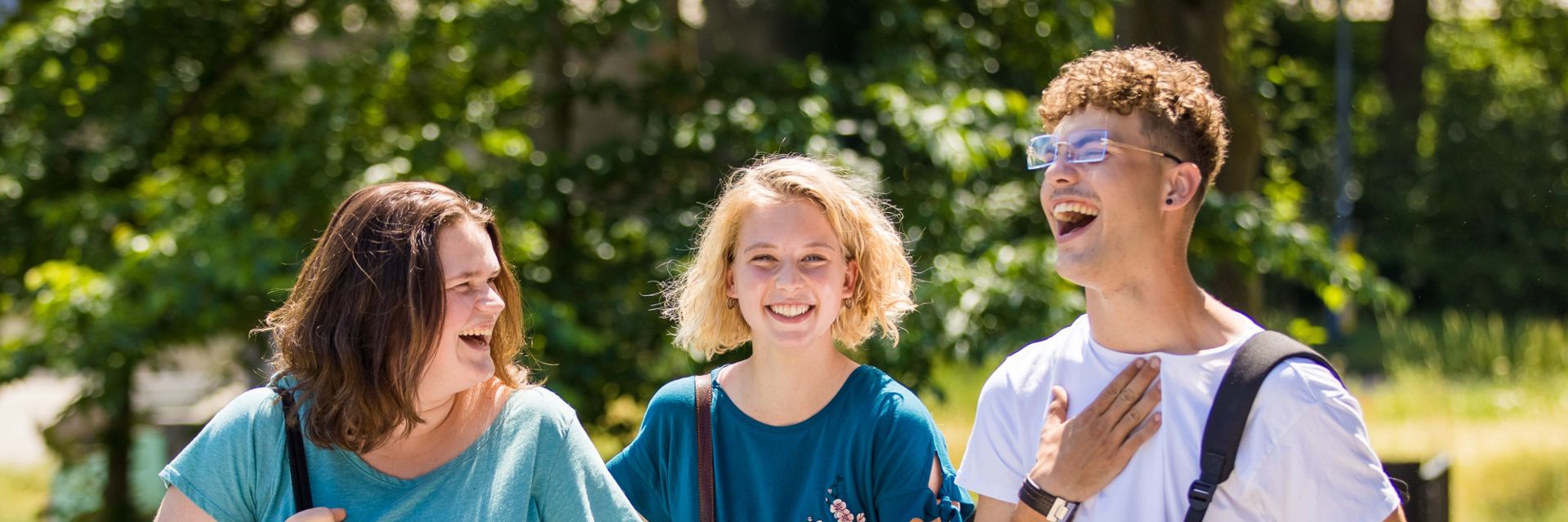 Drie lachende studenten buiten in het groen