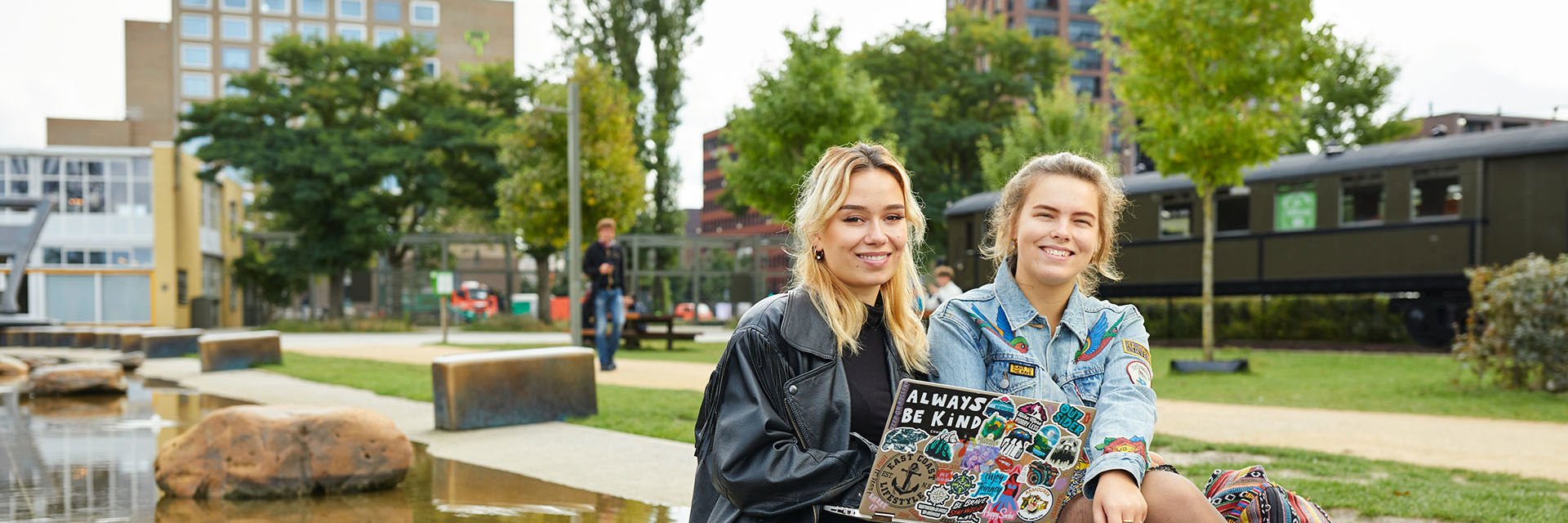 Twee studenten met een laptop, buiten voor een schoolgebouw